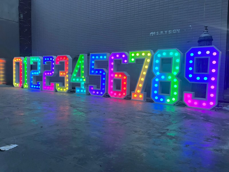Marquee numbers 0 to 9 lit in full-colour RGB bulbs, casting coloured light across the floor